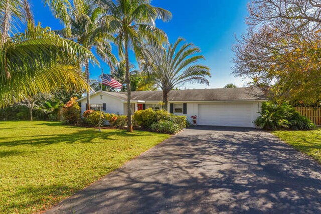 view of front of home featuring driveway, fence, a front yard, and an attached garage