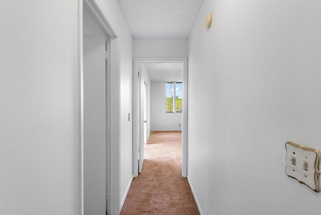 hallway featuring carpet floors, a textured ceiling, and baseboards