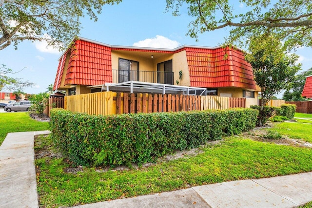 rear view of property featuring a balcony, stucco siding, mansard roof, and fence