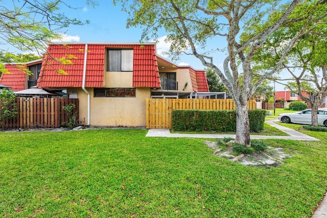 view of front of property with mansard roof, fence, a front yard, and stucco siding