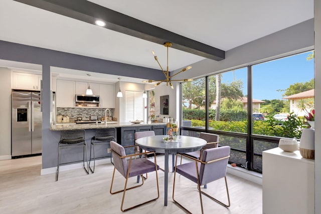 dining space featuring beam ceiling, a healthy amount of sunlight, and light wood-style flooring