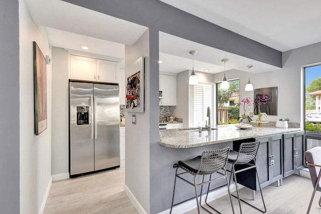 kitchen featuring light stone counters, white cabinets, a sink, baseboards, and stainless steel fridge with ice dispenser