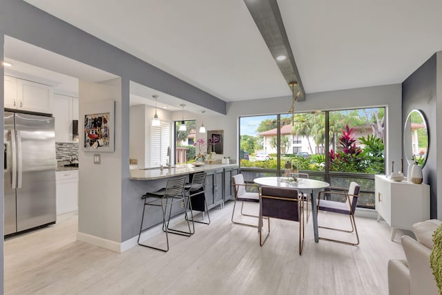dining space featuring beam ceiling, light wood-type flooring, and baseboards