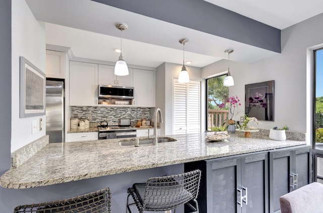 kitchen with backsplash, a sink, appliances with stainless steel finishes, a breakfast bar, and hanging light fixtures