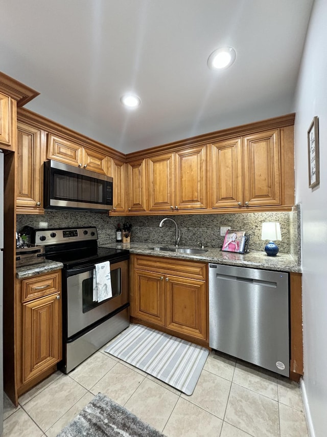 82 Camden Unit D, West Palm Beach, FL 33417 - kitchen featuring stainless steel appliances, a sink, backsplash, brown cabinetry, and stone countertops