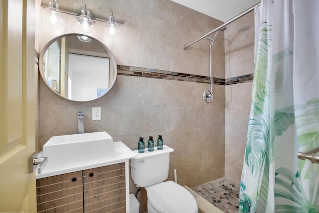 bathroom featuring tiled shower, vanity, toilet, and tile walls