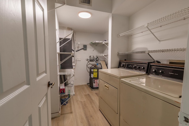laundry room with water heater, laundry area, light wood-style floors, washing machine and clothes dryer, and visible vents