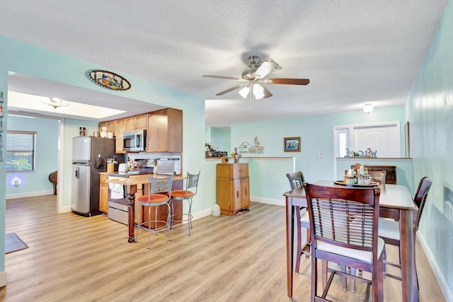 387 Yvonne Dr, West Palm Beach, FL 33406 - dining room featuring light wood-style floors, ceiling fan, baseboards, a textured ceiling, and healthy amount of natural light