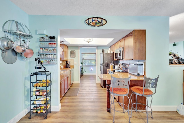 387 Yvonne Dr, West Palm Beach, FL 33406 - kitchen featuring stainless steel appliances, light wood-style flooring, baseboards, a breakfast bar, and a peninsula