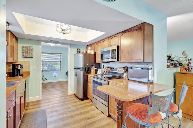 387 Yvonne Dr, West Palm Beach, FL 33406 - kitchen with stainless steel appliances, light wood-style flooring, decorative backsplash, a raised ceiling, and a peninsula
