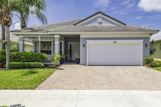 single story home featuring a tiled roof, decorative driveway, a front yard, an attached garage, and stucco siding