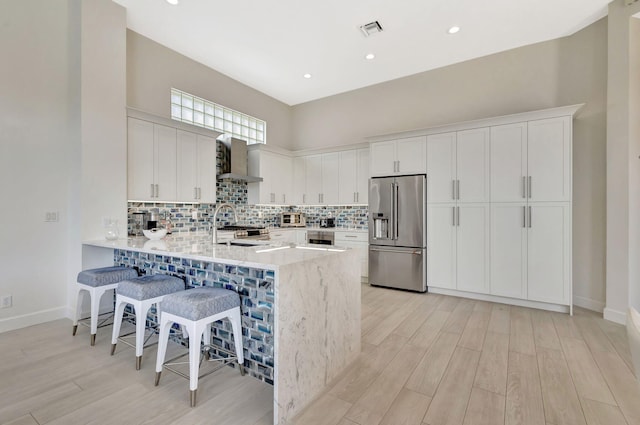 112 Dalena Way, Palm Beach Gardens, FL 33418 - kitchen with a peninsula, light wood-style floors, a breakfast bar area, wall chimney range hood, and high quality fridge