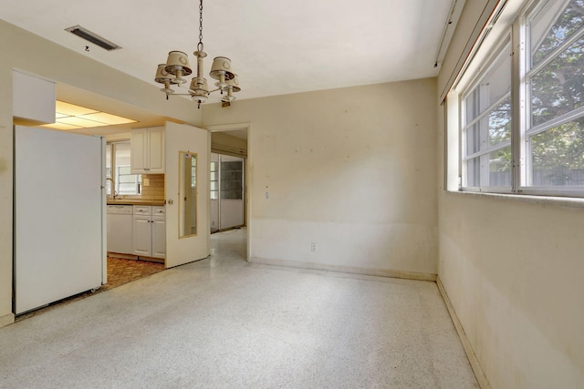 spare room featuring baseboards, a chandelier, visible vents, and light speckled floor