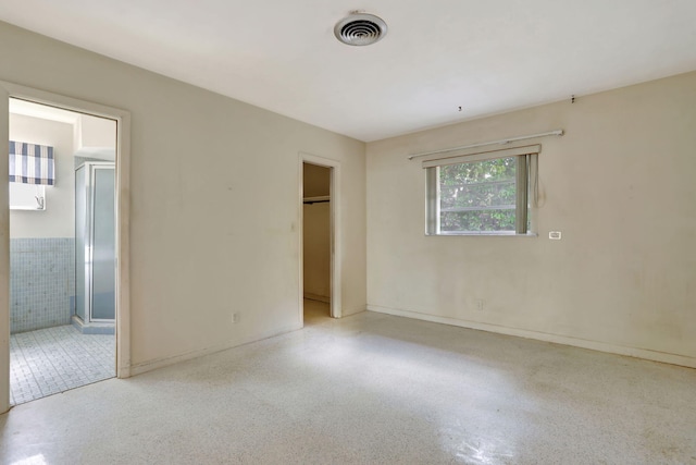 unfurnished bedroom with a walk in closet, visible vents, speckled floor, a closet, and ensuite bathroom