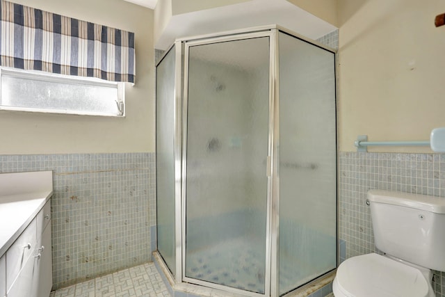 bathroom featuring tile walls, a shower stall, a wainscoted wall, vanity, and toilet