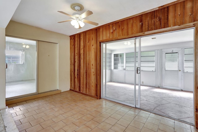 unfurnished room featuring wooden walls, light tile patterned floors, ceiling fan, and a healthy amount of sunlight