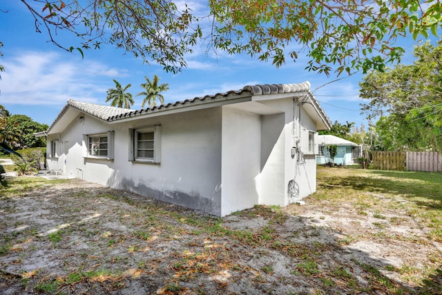 view of side of property with stucco siding, fence, and a tile roof