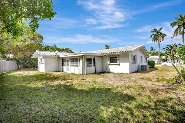 rear view of property featuring central air condition unit, a yard, fence, and stucco siding