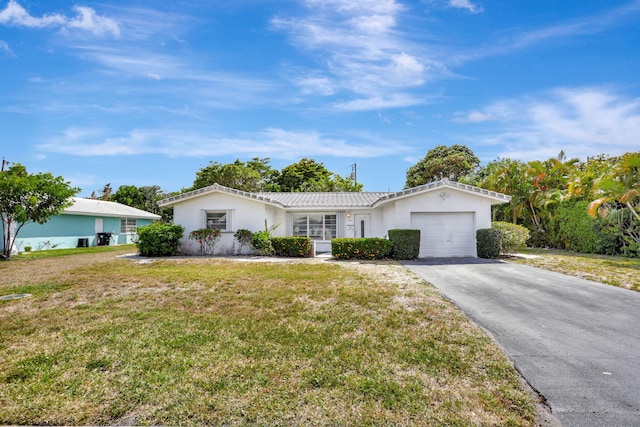 ranch-style home featuring a tile roof, a garage, stucco siding, a front yard, and driveway
