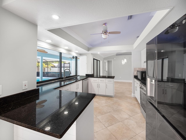 kitchen with appliances with stainless steel finishes, a sink, a ceiling fan, a peninsula, and a tray ceiling