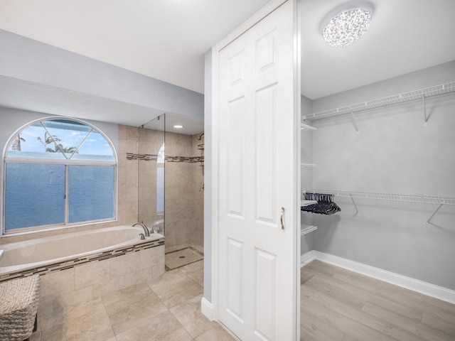bathroom with a spacious closet, a tile shower, and a garden tub