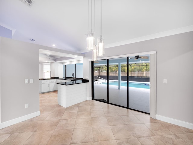 interior space featuring white cabinetry, dark countertops, baseboards, decorative light fixtures, and a peninsula