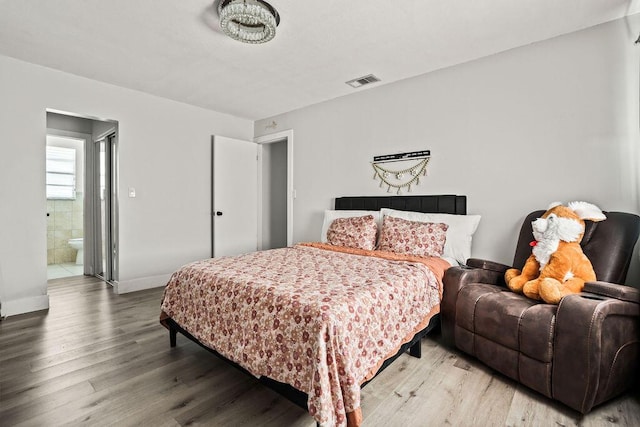 bedroom featuring wood finished floors, visible vents, ensuite bathroom, and baseboards