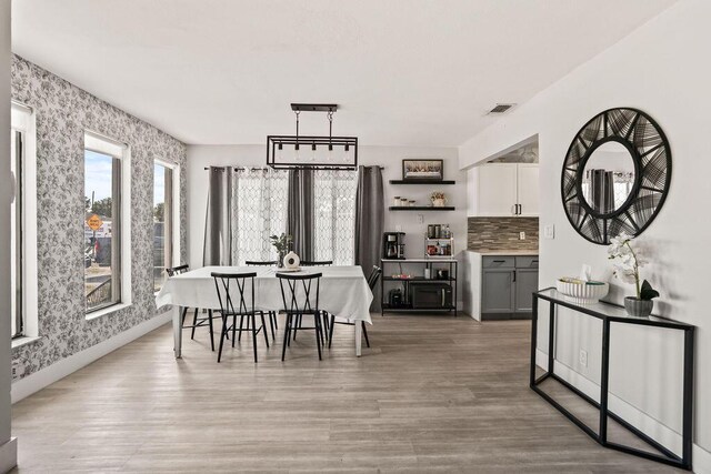 dining space with visible vents, light wood-style flooring, wallpapered walls, and baseboards