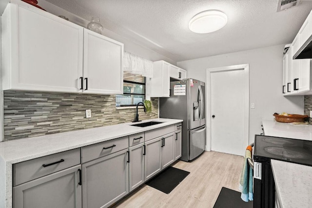 kitchen featuring gray cabinets, light wood-style flooring, stainless steel fridge with ice dispenser, backsplash, and a sink