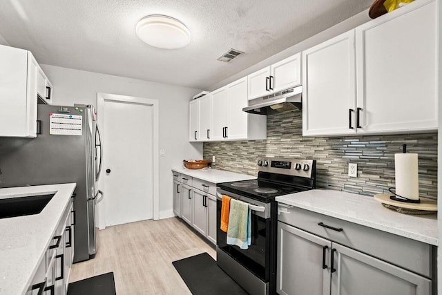 kitchen featuring under cabinet range hood, tasteful backsplash, light wood-type flooring, visible vents, and appliances with stainless steel finishes