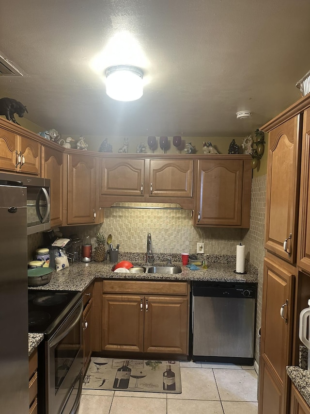 kitchen featuring dark stone counters, light tile patterned floors, decorative backsplash, a sink, and stainless steel appliances