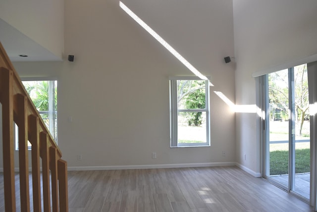 additional living space with a high ceiling, a healthy amount of sunlight, baseboards, and light wood-type flooring