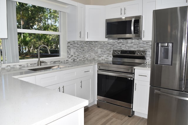 kitchen with stainless steel appliances, white cabinets, backsplash, a sink, and light wood-type flooring