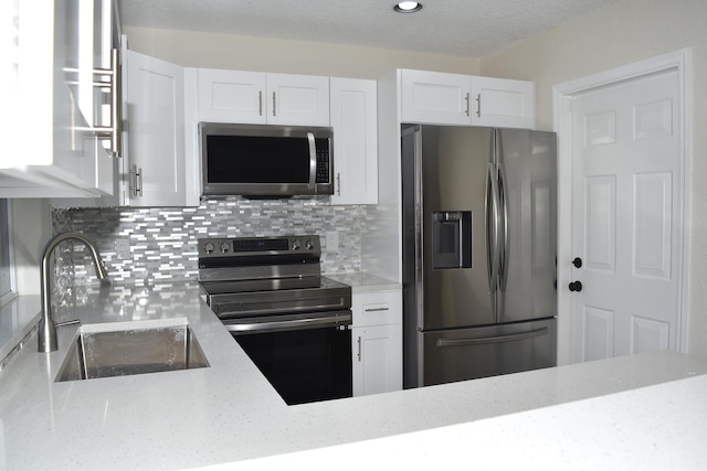 kitchen with light stone countertops, stainless steel appliances, white cabinets, and a sink