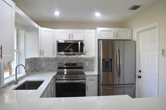 kitchen featuring white cabinets, a sink, appliances with stainless steel finishes, visible vents, and light stone countertops