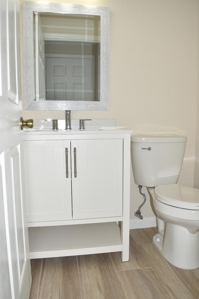 half bath featuring toilet, vanity, wood finished floors, and baseboards