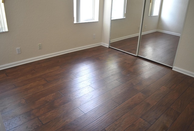 unfurnished bedroom featuring dark wood finished floors, baseboards, and multiple windows