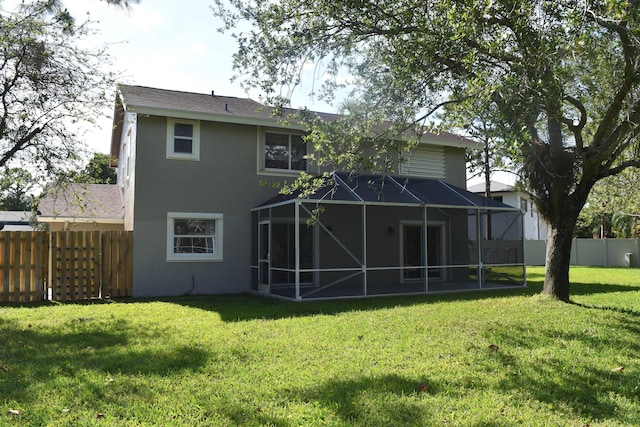 rear view of house featuring fence, glass enclosure, stucco siding, and a yard