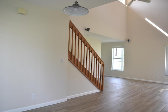 staircase featuring baseboards, wood finished floors, a ceiling fan, and a high ceiling