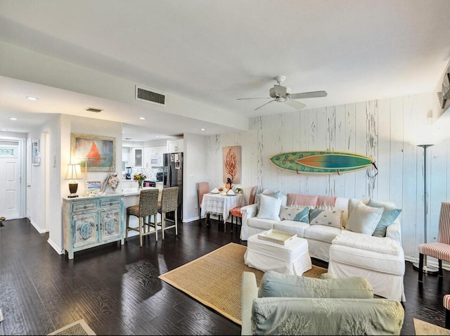 living room featuring ceiling fan, wood walls, baseboards, dark wood-type flooring, and visible vents