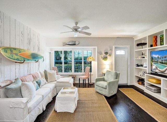living area featuring wood walls, a ceiling fan, wood finished floors, and built in shelves