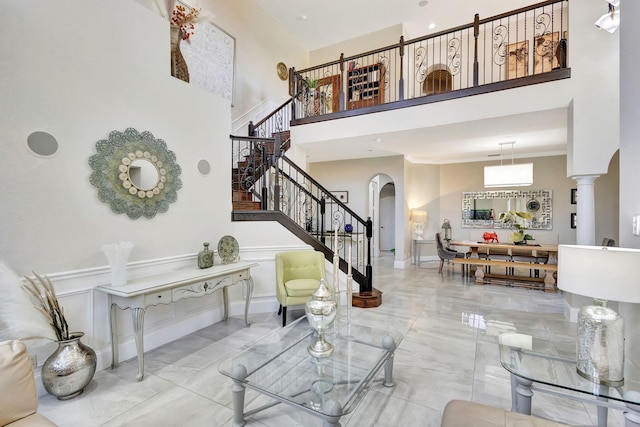 living room featuring stairway, marble finish floor, a decorative wall, a towering ceiling, and arched walkways