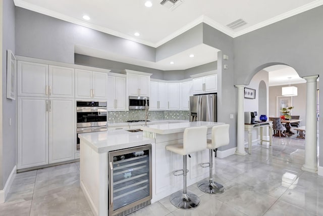 kitchen featuring tasteful backsplash, beverage cooler, visible vents, stainless steel appliances, and arched walkways
