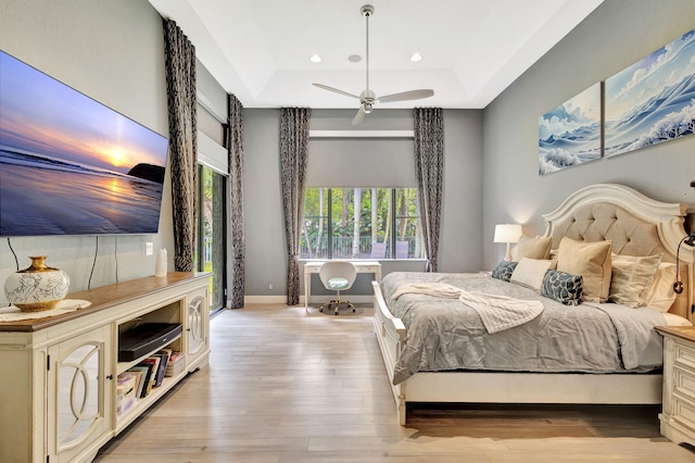 bedroom featuring recessed lighting, ceiling fan, a tray ceiling, light wood-style flooring, and baseboards