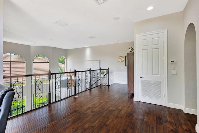 hall with arched walkways, hardwood / wood-style flooring, an upstairs landing, baseboards, and visible vents