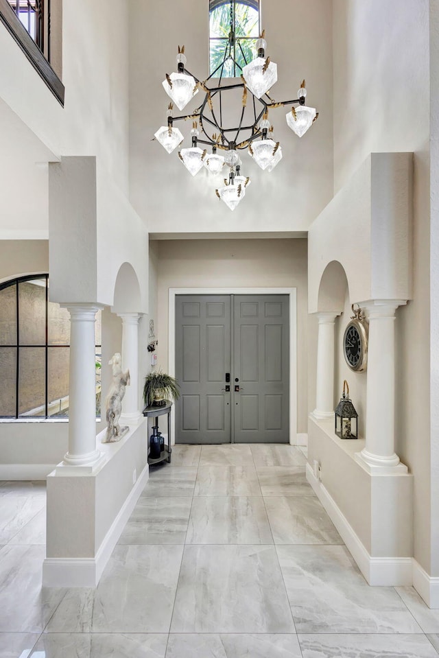 entryway featuring baseboards, an inviting chandelier, decorative columns, marble finish floor, and a high ceiling