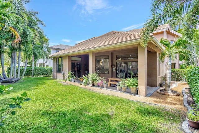 rear view of property featuring stucco siding, a tiled roof, and a lawn