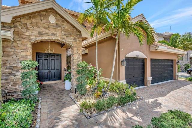 property entrance featuring stucco siding, decorative driveway, an attached garage, and stone siding