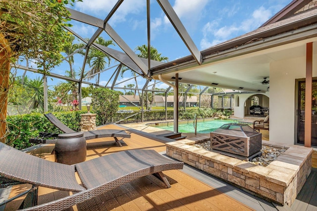 view of patio / terrace with a fire pit, glass enclosure, a ceiling fan, and an outdoor pool