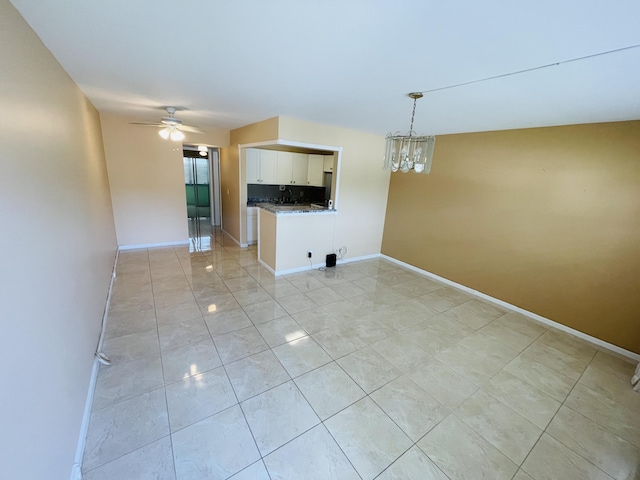interior space featuring ceiling fan with notable chandelier and baseboards